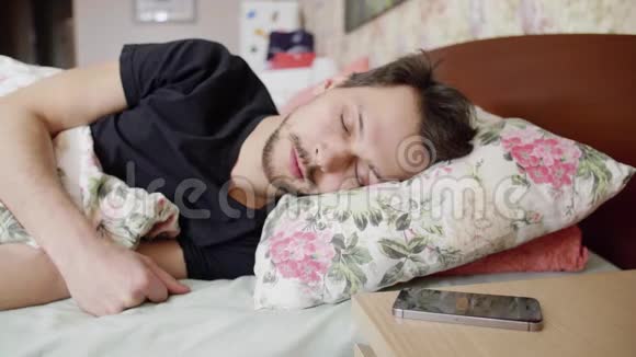 深色头发的男人躺在床上枕头和手机放在床头柜上视频的预览图