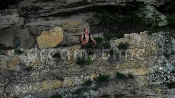 从空中俯瞰一个旅行者背包坐在岩石中的架子边缘向远处望去4K视频的预览图