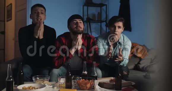 三个朋友在家看电视上的足球赛时祈祷为最好的足球队加油感情男子视频的预览图