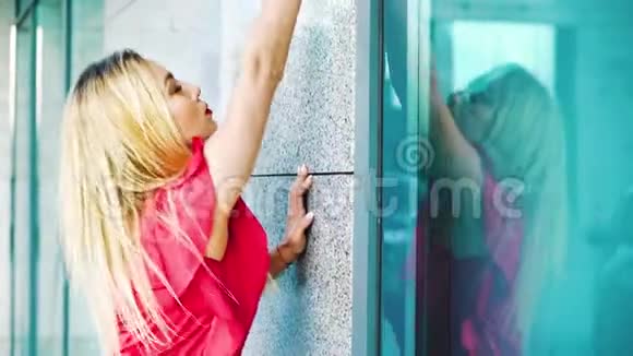 漂亮的金发女郎穿着鲜艳的服装在外面的现代建筑附近跳舞视频的预览图