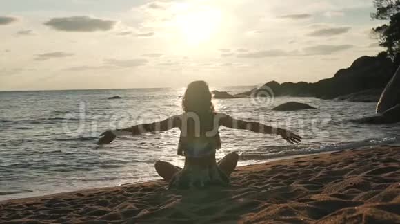 女孩举起双手坐在海边的沙滩上视频的预览图