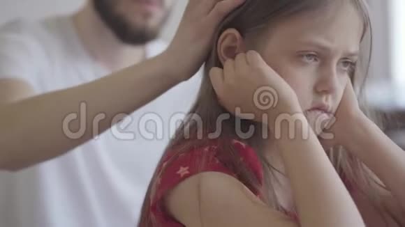特写一幅悲伤的小女孩坐在前景上的肖像双手紧紧地抱着她的头他的父亲视频的预览图