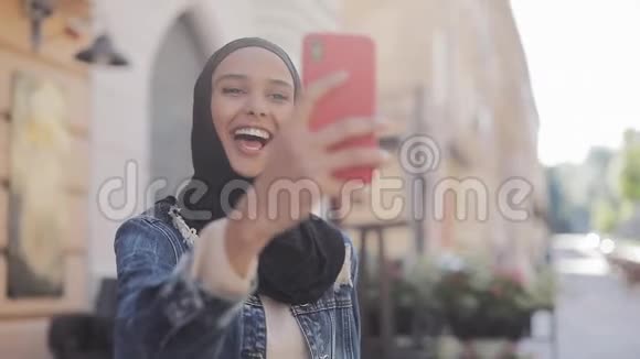 年轻的穆斯林妇女戴着头巾在美丽的城市旅行时用照相机打视频电话的肖像视频的预览图