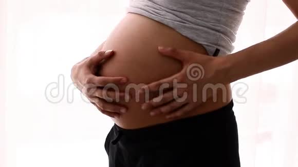 年轻的欧洲孕妇在白色背景下轻轻抚摸她裸露的大肚子视频的预览图