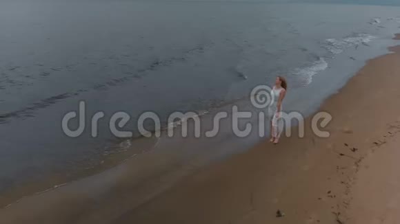 空中侧景美丽的金发女郎在海边漫步一位穿着白色连衣裙的海滩仙女与视频的预览图