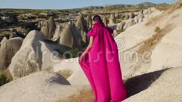 穿着紫色长裙的女孩站在卡帕多西亚的岩石上视频的预览图