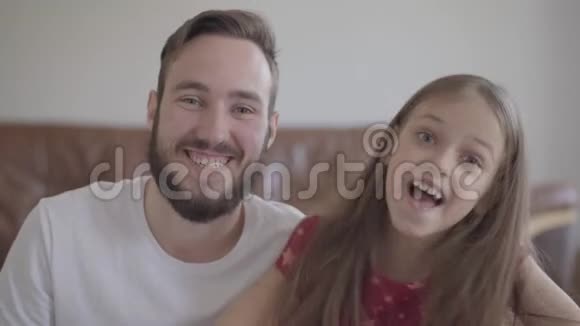 英俊的胡子男和可爱的积极女孩看着镜头微笑孩子把头靠在男人身上视频的预览图
