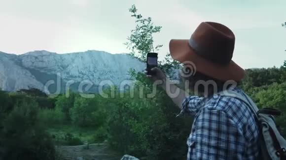 一个年轻人在山林中徒步旅行在智能手机上拍一张山的照片积极主动视频的预览图
