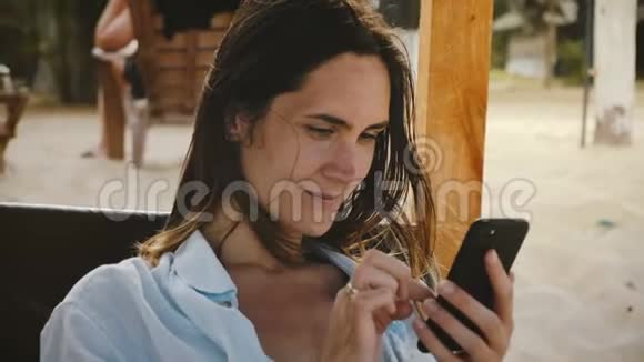 美丽的电影镜头快乐的年轻女子使用智能手机电子商务应用程序微笑放松休息在海滩椅子视频的预览图