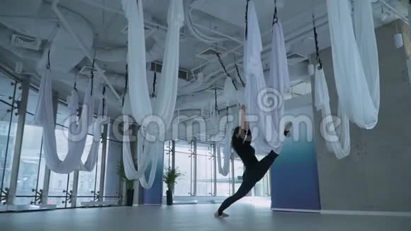 美丽的女人做腿部伸展运动把一条腿放在吊床上做瑜伽另一条腿放在室内工作室的地板上视频的预览图