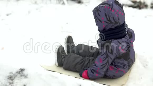一个孩子在雪地滑梯上翻滚冬天在街上玩在寒冷的冬天孩子穿着一件夹克和一件视频的预览图