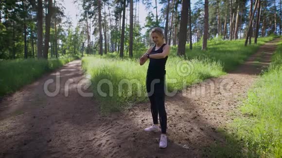 一位年轻女子手上拿着一只智能手表想知道她在一个温暖的公园里跑了多少公里视频的预览图