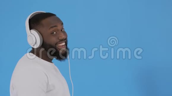 一位年轻的美国黑人青年带着耳机听音乐在蓝色的上空唱歌视频的预览图