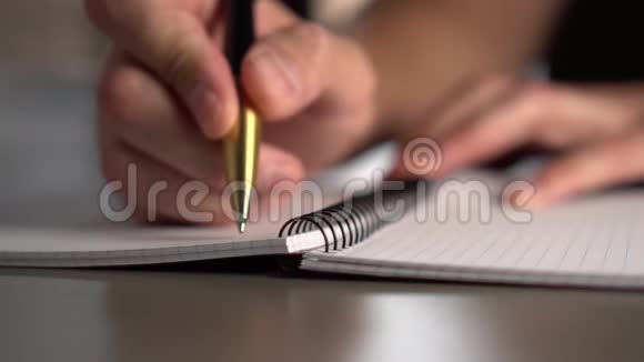 一个男人用一支黄色的黑色钢笔在灰色桌子上的笔记本上写字窗外的光线照亮了工作场所视频的预览图