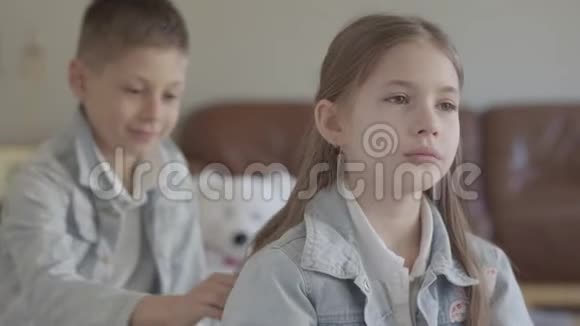 双胞胎兄弟淘气的男孩在舒适的客厅里玩着拉扯他可爱妹妹的头发和微笑视频的预览图