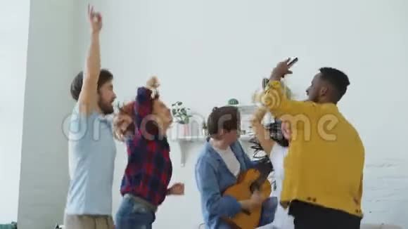 一群多民族的朋友跳舞年轻人弹吉他在室内举行家庭聚会视频的预览图