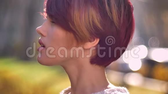 年轻的白种人粉红头发女孩的特写肖像转向相机平静地微笑在秋天公园的背景视频的预览图