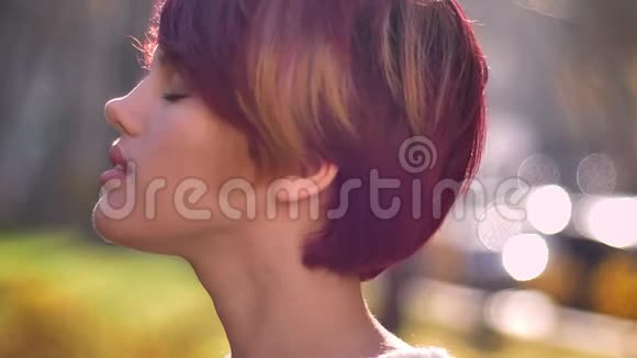 在秋天公园里年轻的白种人粉红色头发的女孩转向相机困惑地看着她的特写肖像视频的预览图