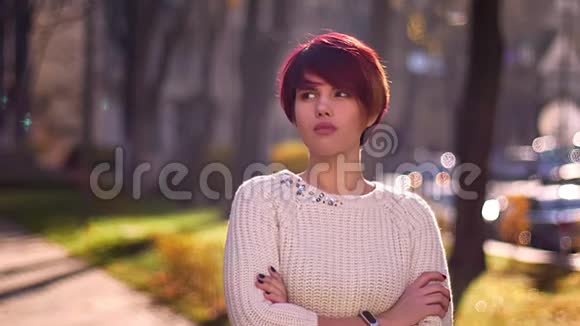 年轻的白种人粉红头发女孩的肖像双臂交叉平静地注视着公园里的镜头视频的预览图