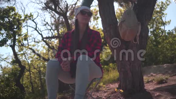 一个黑发女孩穿着一件黑色和红色的衬衫一个手帕和眼镜坐在森林里环顾四周视频的预览图