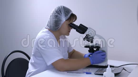 实验室技术员看着显微镜写下数据视频的预览图