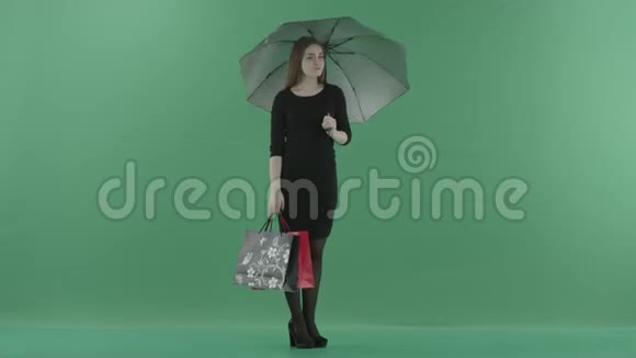 穿着黑色小裙子的漂亮女人正站在一把带购物袋的伞下她站在一边视频的预览图