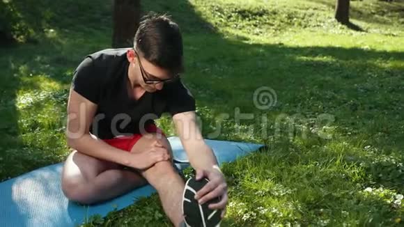 漂亮的年轻人戴着眼镜一大早在一个美丽的绿色公园里伸腿户外活动在视频的预览图