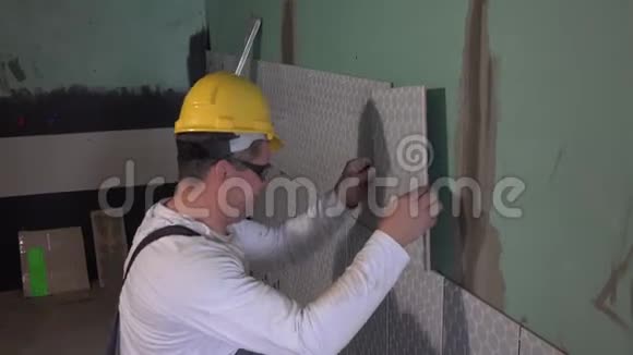 戴着黄色头盔的熟练工人在墙上铺上瓷砖看着摄像机视频的预览图