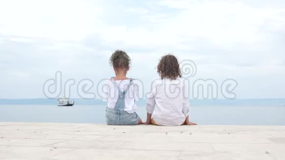 可爱的孩子们一个男孩和一个女孩坐在海湾岸边的码头上看着对方青少年视频的预览图