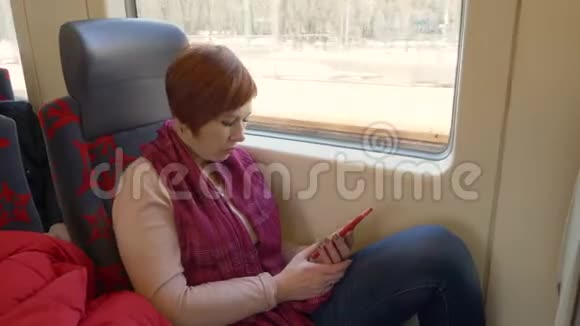 在火车上坐在窗口背景下的旅行女性看着智能手机视频的预览图