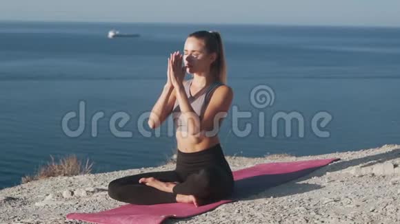 女人坐在垫子上的莲花瑜伽姿势在户外冥想慢动作视频的预览图