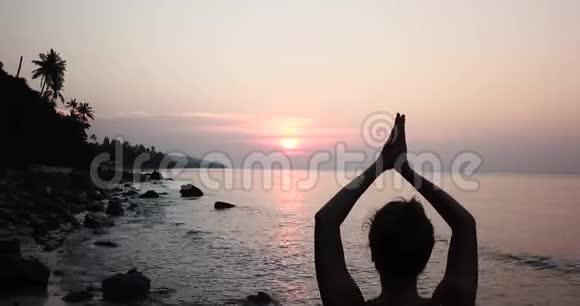 日落时静海石岸瑜伽的女性剪影视频的预览图