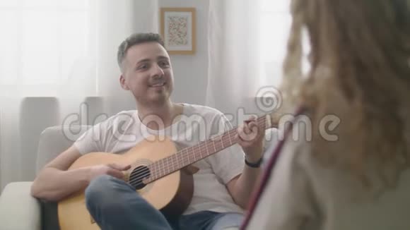 在一个舒适的客厅里手持的男人为他的女朋友弹吉他视频的预览图