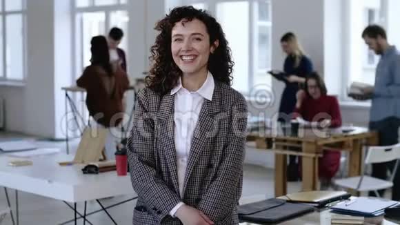 中等肖像的年轻白种人商务女性卷发正式西装微笑在相机在现代办公室视频的预览图