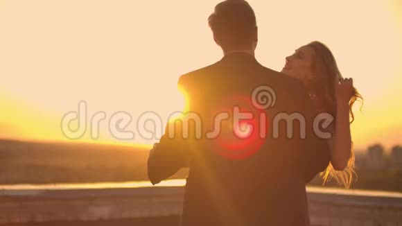 两个情人在日出日落时在俯瞰城市的摩天大楼上拥抱跳舞浪漫的场景视频的预览图
