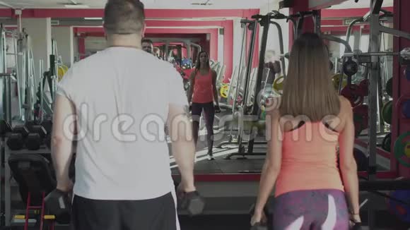有个人教练的肥胖男人在健身房里用哑铃做身体抽搐超重的男性和女性教练燃烧视频的预览图