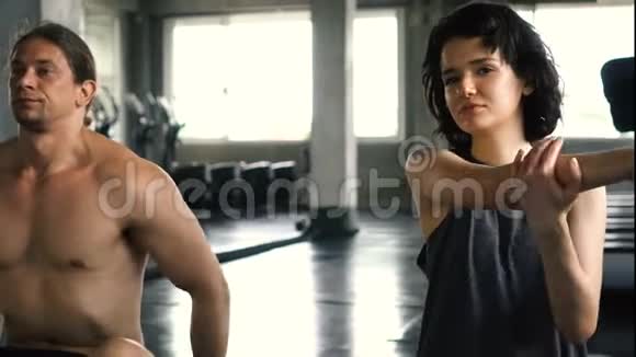 年轻的女人和男人在健身房地板上伸展手臂两个人在室内工作视频的预览图