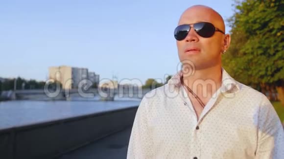 戴墨镜的秃头成年男子穿过湖上的公园看着前方视频的预览图