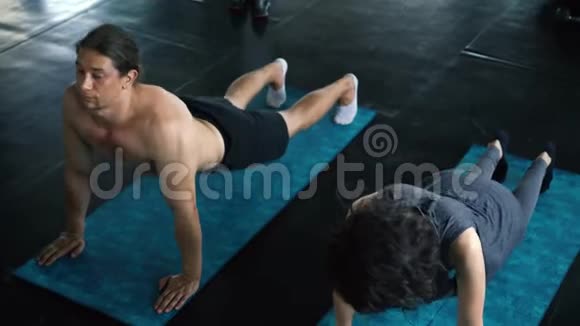 年轻的女人和男人在健身房地板上用向下的狗姿势练习瑜伽两个人在室内工作视频的预览图