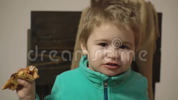 饿孩子吃披萨穿绿色毛衣的男孩坐在木椅上吃披萨概念视频的预览图