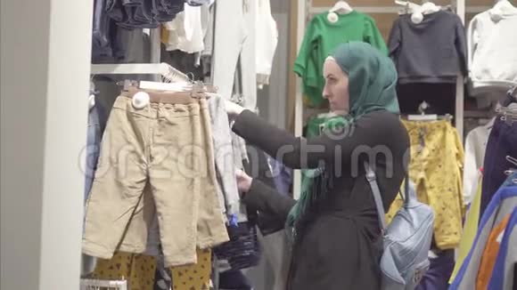 穿着头巾和背包的穆斯林妇女在儿童商店挑选衣服视频的预览图
