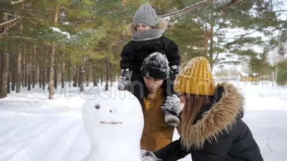 年轻的家庭妈妈儿子和爸爸正在冬季城市公园堆雪人视频的预览图