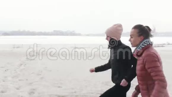 两个微笑的女人在雪地海滩上奔跑视频的预览图