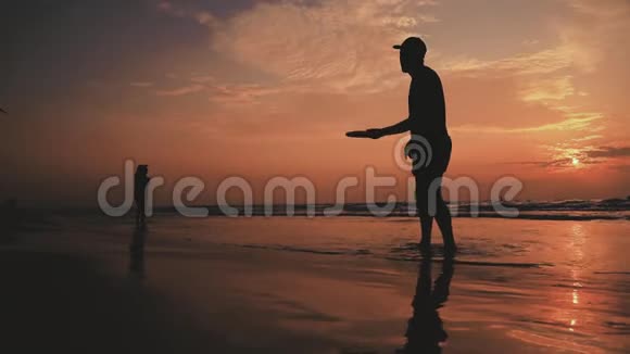 下面的动作在沙滩上玩飞盘的剪影人们被夏日的阳光照得背光视频的预览图