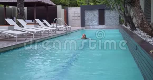 酒店庭院里可爱的室外游泳池周围是热带丛林女孩在孤独中游泳视频的预览图