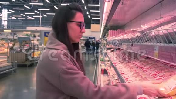 在超市里戴眼镜和外套的年轻女人选择了一包鸡肉视频的预览图