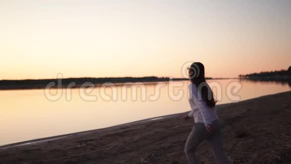 一个年轻的女人在春天的河滩上享受金色时光的日落视频的预览图