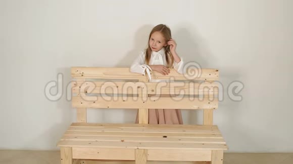 可爱的小女孩在工作室里摆姿势旁边是一张白色背景的木凳视频的预览图