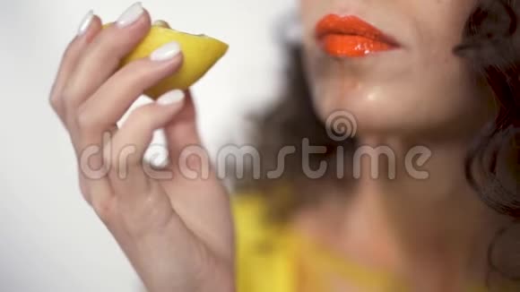 用明亮的橙色口红贴近湿润丰满的嘴唇愉快地咬着一块酸柠檬慢动作视频的预览图