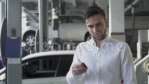 汽车服务商店里的一位年轻的帅哥在车的背景上展示着他的车钥匙微笑着视频的预览图